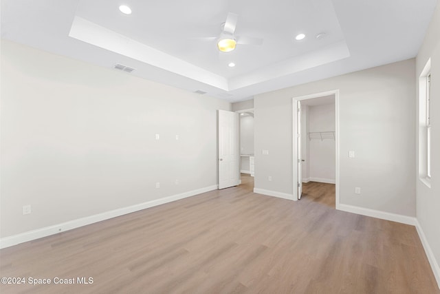 unfurnished bedroom with a spacious closet, ceiling fan, a raised ceiling, light hardwood / wood-style floors, and a closet