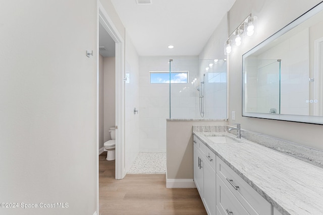 bathroom featuring a tile shower, hardwood / wood-style floors, vanity, and toilet