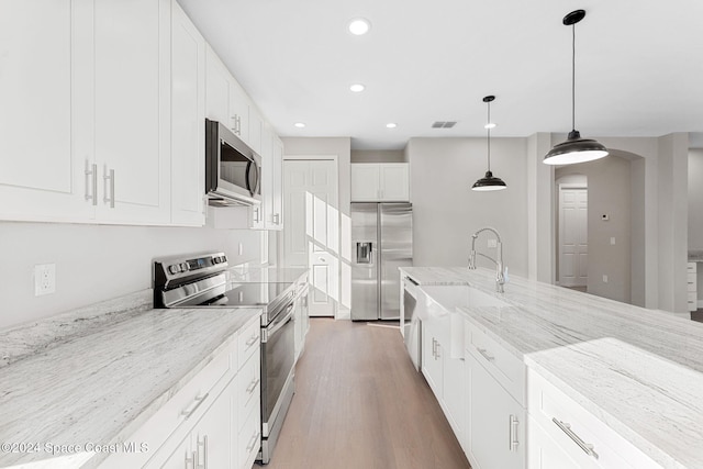 kitchen featuring hanging light fixtures, light stone counters, hardwood / wood-style floors, white cabinets, and appliances with stainless steel finishes