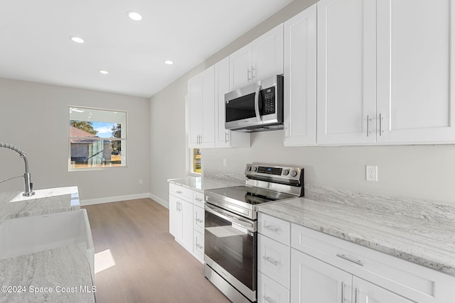 kitchen with sink, stainless steel appliances, light stone counters, white cabinets, and light wood-type flooring