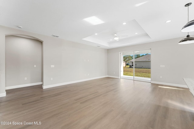 unfurnished room with ceiling fan, a raised ceiling, and wood-type flooring