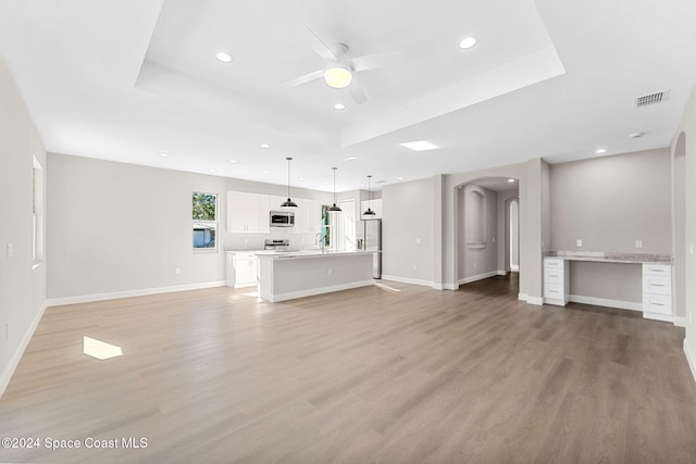 unfurnished living room featuring ceiling fan, light hardwood / wood-style floors, built in desk, and a tray ceiling