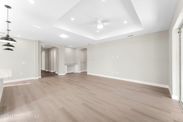 unfurnished living room featuring light hardwood / wood-style floors, a raised ceiling, and ceiling fan