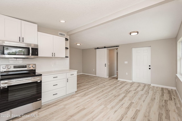 kitchen with white cabinets, a barn door, light hardwood / wood-style floors, and stainless steel appliances