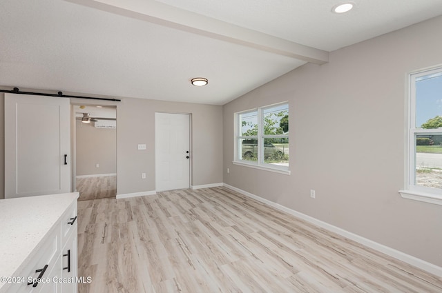 unfurnished bedroom with vaulted ceiling with beams, a barn door, light hardwood / wood-style flooring, and multiple windows