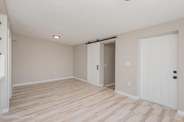 unfurnished bedroom with a barn door, light wood-type flooring, a textured ceiling, and a closet