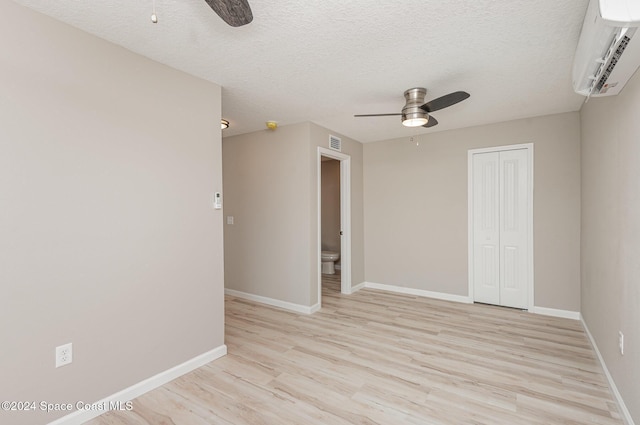 spare room with a wall unit AC, ceiling fan, light hardwood / wood-style floors, and a textured ceiling