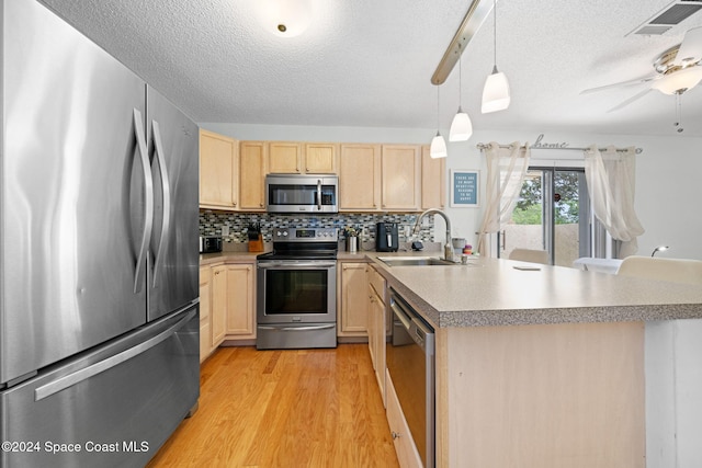 kitchen featuring stainless steel appliances, sink, light brown cabinets, decorative light fixtures, and light hardwood / wood-style floors