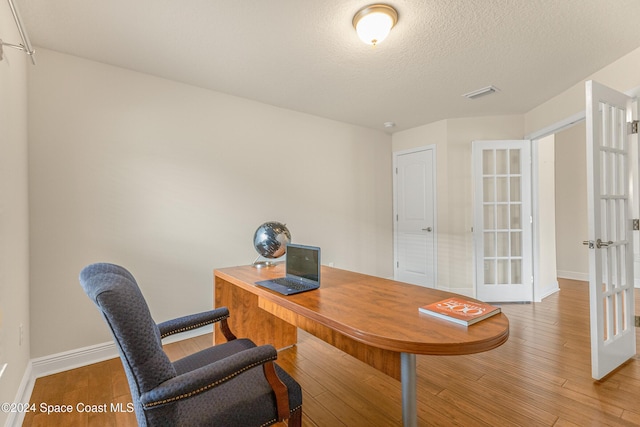 home office with french doors, hardwood / wood-style floors, and a textured ceiling