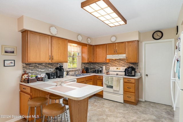 kitchen with sink, a breakfast bar area, kitchen peninsula, white appliances, and backsplash