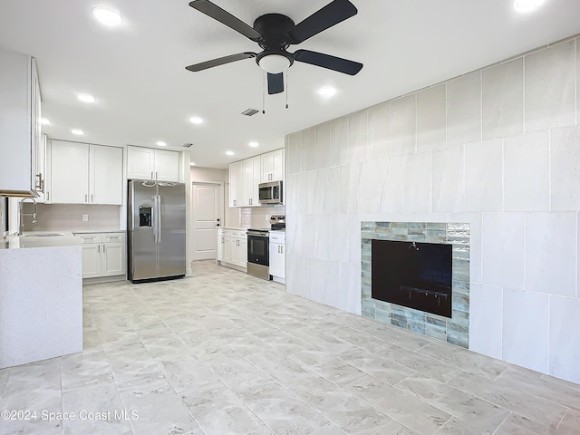 kitchen with a tile fireplace, white cabinetry, sink, ceiling fan, and appliances with stainless steel finishes