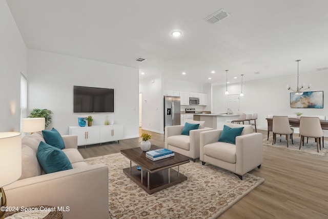 living room featuring an inviting chandelier, sink, and light hardwood / wood-style flooring