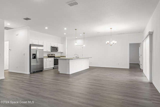 kitchen featuring appliances with stainless steel finishes, dark wood-type flooring, decorative light fixtures, white cabinets, and an island with sink