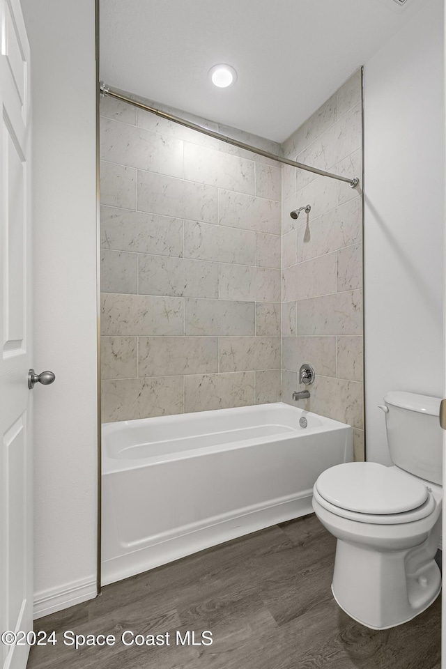 bathroom with hardwood / wood-style flooring, toilet, and tiled shower / bath