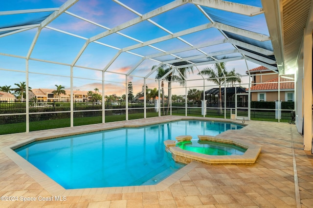 pool at dusk with a lawn, a lanai, an in ground hot tub, and a patio