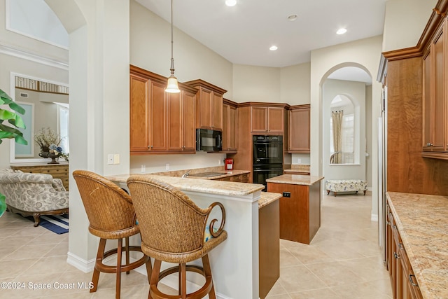 kitchen featuring a kitchen breakfast bar, light stone counters, black appliances, a high ceiling, and a kitchen island