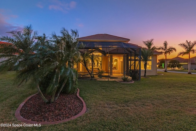 back house at dusk featuring a lanai and a lawn