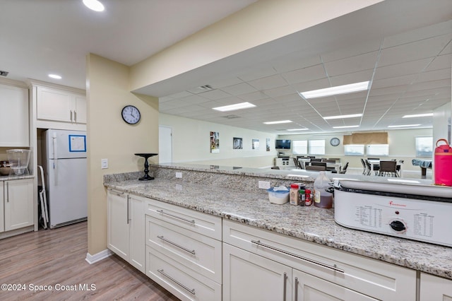 kitchen with white cabinets, white refrigerator, light stone countertops, and light wood-type flooring