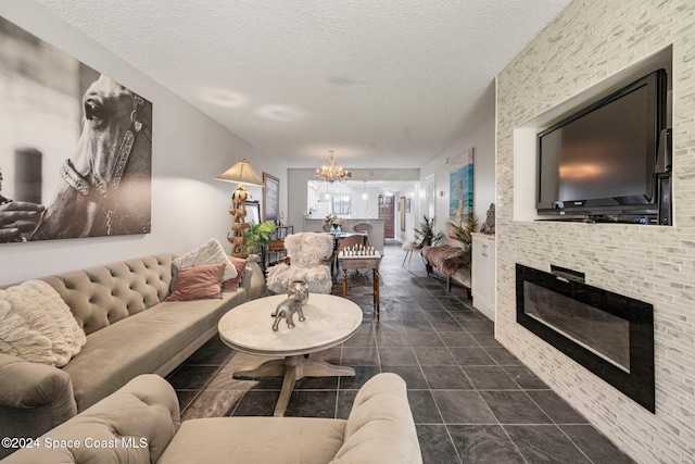 living room featuring a textured ceiling, a fireplace, dark tile patterned flooring, and a chandelier