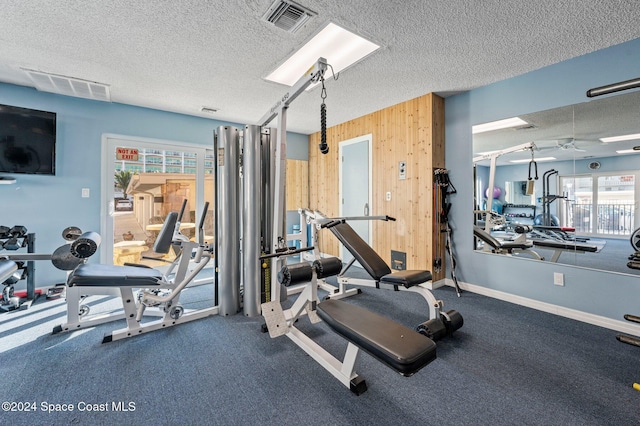 workout area featuring ceiling fan, a textured ceiling, and wooden walls