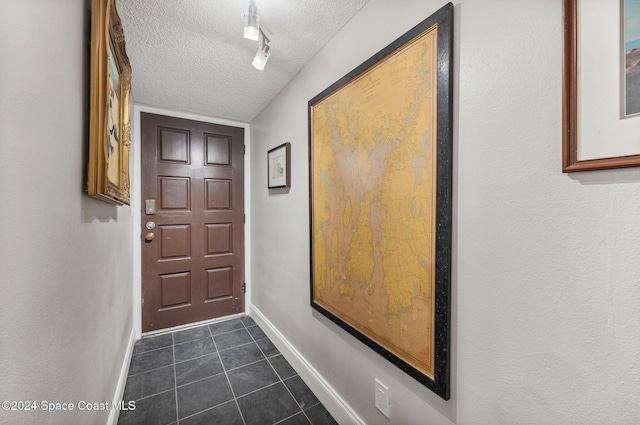 entryway with dark tile patterned floors, track lighting, a textured ceiling, and baseboards