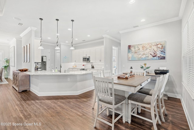 kitchen with dark wood-type flooring, hanging light fixtures, an island with sink, appliances with stainless steel finishes, and white cabinetry