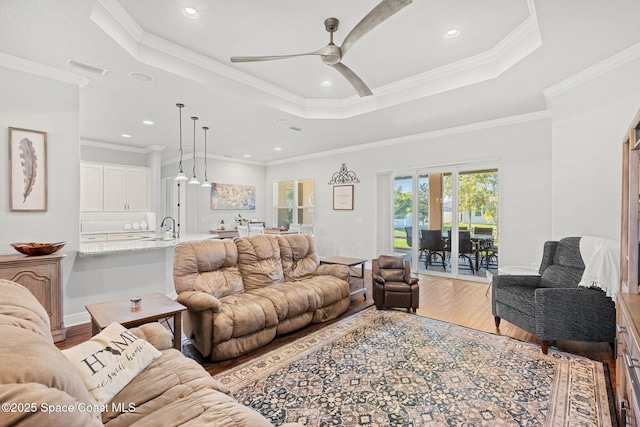 living room with a tray ceiling, ceiling fan, ornamental molding, and light hardwood / wood-style floors