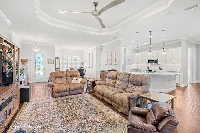 living room with a tray ceiling, light hardwood / wood-style floors, and ornamental molding