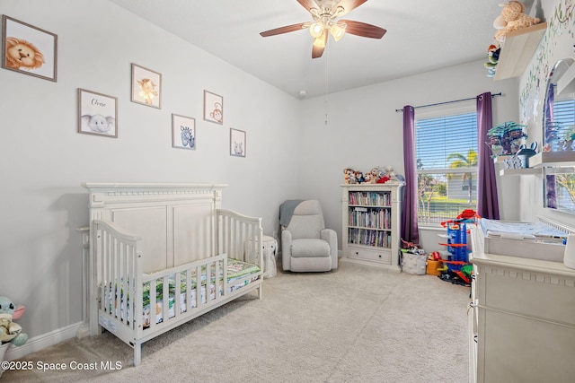 bedroom featuring a crib, light colored carpet, and ceiling fan