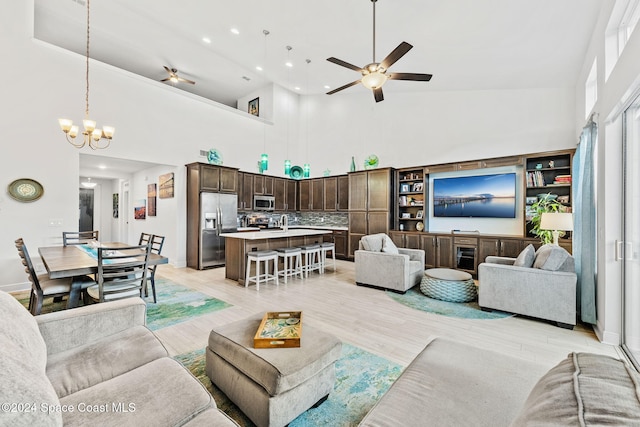 living room with a high ceiling, ceiling fan with notable chandelier, and light hardwood / wood-style flooring