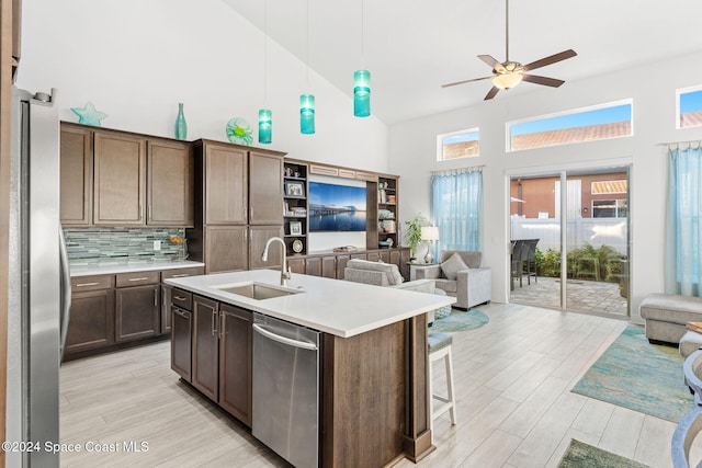 kitchen featuring decorative backsplash, a center island with sink, stainless steel appliances, and dark brown cabinets