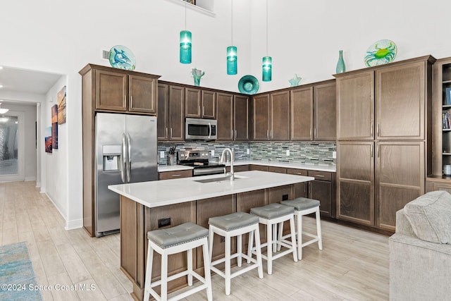 kitchen with sink, a high ceiling, pendant lighting, a kitchen island with sink, and appliances with stainless steel finishes