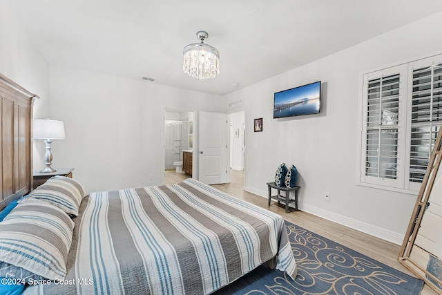 bedroom featuring connected bathroom, wood-type flooring, and a notable chandelier