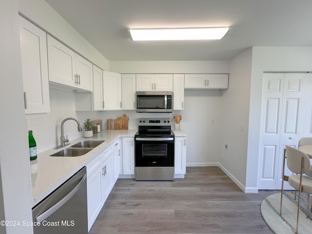 kitchen featuring light stone countertops, white cabinetry, sink, light hardwood / wood-style flooring, and appliances with stainless steel finishes