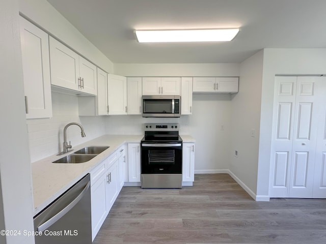 kitchen with appliances with stainless steel finishes, light stone counters, sink, light hardwood / wood-style floors, and white cabinetry