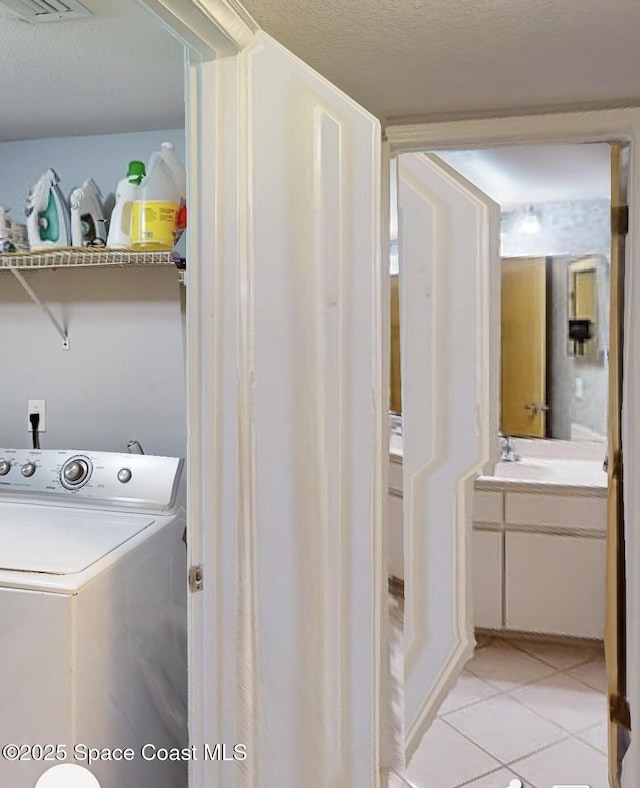 clothes washing area featuring washer / dryer, a textured ceiling, and light tile patterned floors