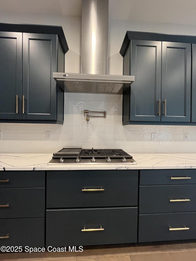 kitchen featuring light stone counters, stainless steel gas stovetop, exhaust hood, and tasteful backsplash