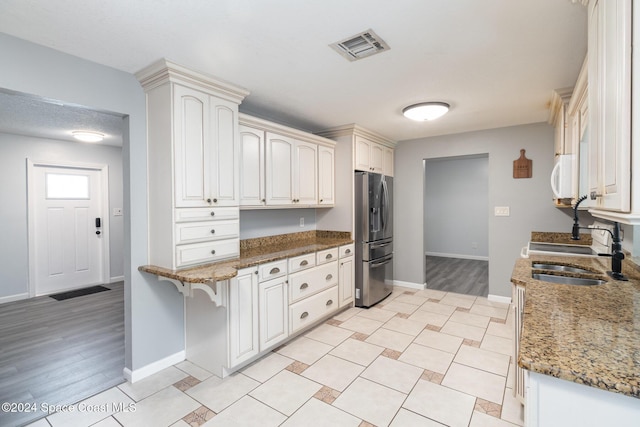 kitchen featuring white cabinetry, sink, dark stone counters, and stainless steel refrigerator with ice dispenser