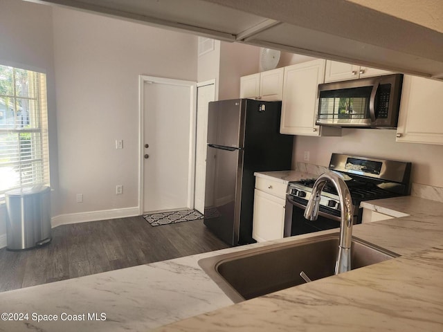 kitchen with light stone counters, stainless steel appliances, sink, white cabinets, and dark hardwood / wood-style floors