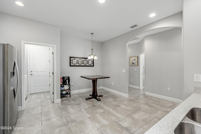 interior space featuring pendant lighting, stainless steel fridge, light tile patterned floors, a notable chandelier, and light stone counters