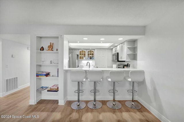 kitchen featuring built in features, appliances with stainless steel finishes, light hardwood / wood-style floors, a kitchen bar, and kitchen peninsula