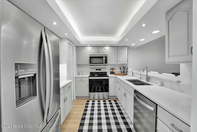 kitchen with white cabinetry, sink, stainless steel appliances, a raised ceiling, and light wood-type flooring