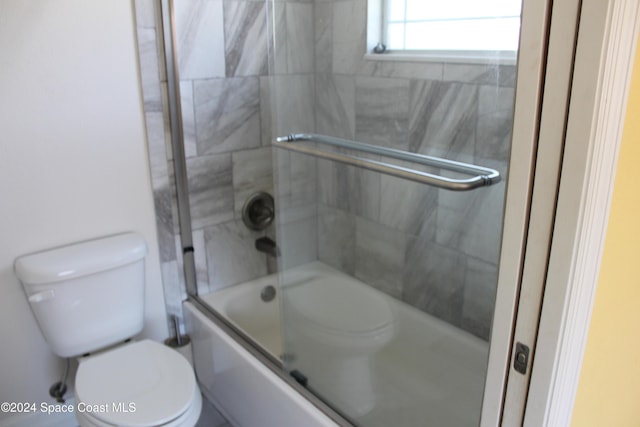 bathroom featuring toilet and bath / shower combo with glass door