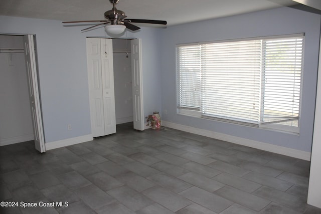 unfurnished bedroom featuring multiple windows, ceiling fan, and two closets