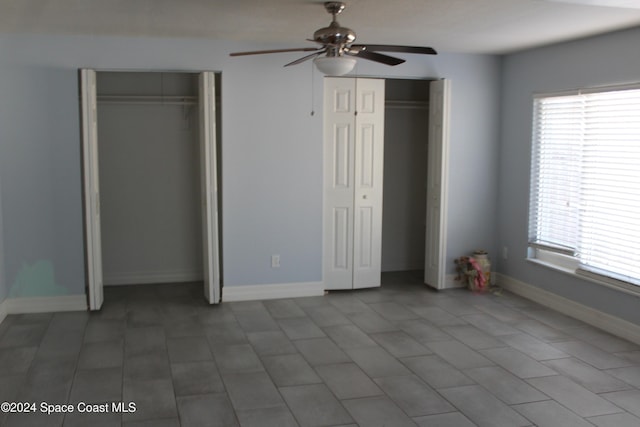 unfurnished bedroom with multiple windows, two closets, tile patterned floors, and ceiling fan