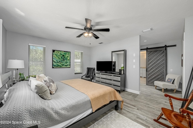 bedroom with ceiling fan, a barn door, and light hardwood / wood-style floors