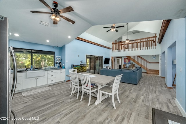 dining space with ceiling fan, light wood-type flooring, sink, and high vaulted ceiling