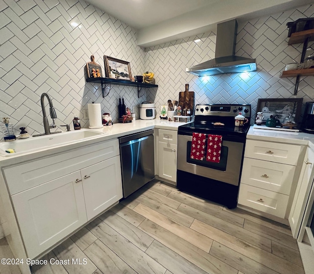 kitchen with sink, wall chimney exhaust hood, light hardwood / wood-style floors, white cabinets, and appliances with stainless steel finishes