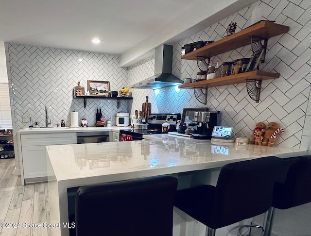 kitchen featuring kitchen peninsula, wall chimney exhaust hood, light hardwood / wood-style floors, white cabinetry, and stainless steel appliances