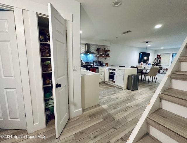 interior space with stainless steel range with electric cooktop, white cabinets, hanging light fixtures, decorative backsplash, and light hardwood / wood-style floors